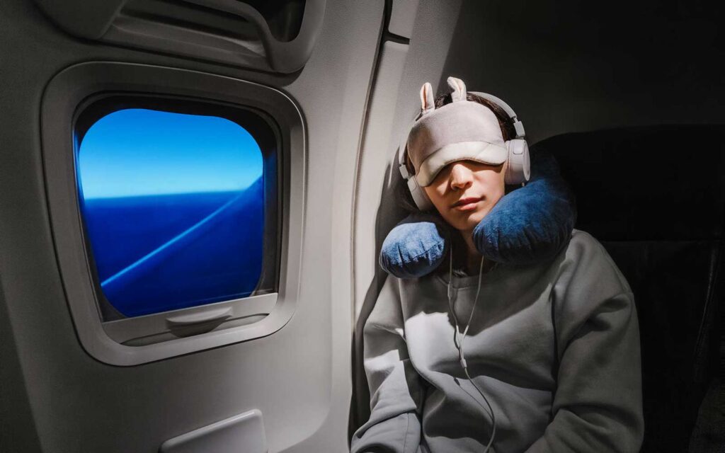 a person wearing a mask and headphones sitting in an airplane Prevent Jet Lag.